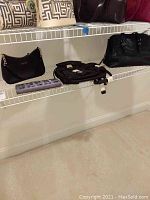 Black purses and backpacks on wire shelves including the Calvin Klein purse and London Fog backpack