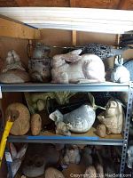 Shelf with various lawn figures including birds, rabbits, and owls made of plaster and other materials.