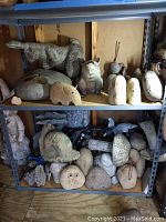 Full view of multiple stone garden statues on metal shelves including rabbit, pig, butterfly, mushroom, owl, and other animals in weathered condition