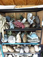 Shelving unit with multiple garden statues including girl figure, rabbits, owls, frog, turtle and decorative metal flower stake.