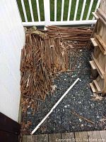 Pile of rusty steel rebar of various sizes stacked against a white wall on gravel surface under a white railing.