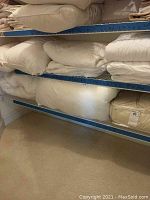 Shelving with folded mattress covers and rolled pillows in beige and white colors
