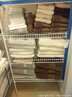 Wire shelving with multiple stacks of folded bath towels and washcloths in white, cream, brown and purple
