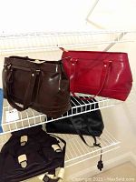 Two Monsac handbags, dark brown and dark red, on a metal rack showing front and side views