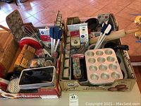 Wide view showing the full assortment of bakeware, utensils, cookie cutters, and various baking accessories packed inside two cardboard boxes.