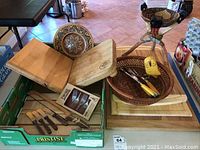 Photo of the lot showing wooden cutting boards, utensils, a boxed set of forks, and a footed decorative bowl with a yellow duck inside.