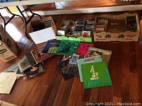 Wide view showing contents of lot including vinyl albums on floor and rows of CDs and DVDs in cardboard boxes underneath a table.
