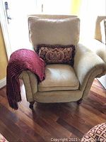 Front view of the beige Paul Robert armchair showing the burgundy throw draped over left arm and decorative pillow on seat.