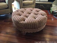 Full view of the round ottoman placed on wooden floor, showing patterned upholstery and tufted top.