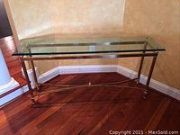 Glass top sofa table with brass frame and four cylindrical legs.