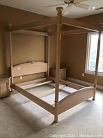 Full view of the four poster bed frame set up in a room showing light wood, posts, and headboard shape.