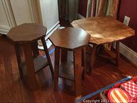 Wooden side table with discoloration and two wooden plant stands with scratches placed on hardwood floor.