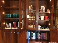 Coffee mugs on cabinet shelves including Disney and Winnie the Pooh themed mugs, insulated travel mugs, glasses in three sizes, Dunkin Donuts water bottle, and white coffee carafe.