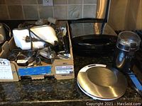 Wide view of lot showing KitchenAid hand mixer, kitchen utensils in box, Salter kitchen scale, Maxim coffee grinder, and Mickey Mouse waffle iron on the kitchen counter