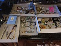 Overview of nine watches and costume jewelry in four trays on countertop