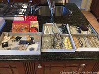 Overview showing three trays with necklaces, earrings, and jewelry bags on kitchen counter.