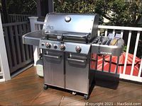 Front view of stainless steel Weber Genesis propane grill with three control knobs, lower cabinet doors, side shelves and propane tank behind