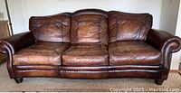Front view of three-seat brown leather couch showing rolled arms, nailhead trim and bun feet