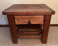Front view of a solid pine wood side table with thick legs, one drawer with metal handle, and a slatted shelf underneath.