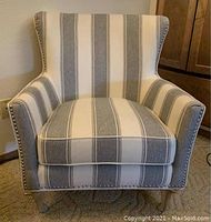 Front view of the armchair showing striped upholstery, nailhead trim, and wooden legs
