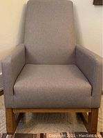Front view of the gray fabric rocking chair showing straight armrests, cushioned seat and high backrest, wood frame bottom.