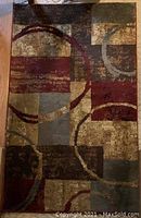 Photo showing rectangular abstract carpet with geometric and circular patterns in browns, burgundy, beige, and grey colors.