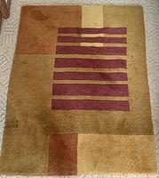Photo of rectangular wool carpet with geometric design; horizontal maroon stripes and solid color blocks in browns and tans