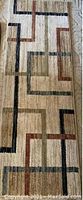 Photo of a 2x6 feet rectangular carpet with abstract geometric line patterns in brown, black, rust, and olive on beige background.