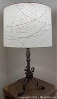 Wrought iron table lamp with white drum shade featuring a subtle geometric pattern of curved, intersecting lines.