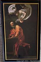 Framed print of Caravaggio's The Inspiration of Matthew showing seated man in orange robe writing and angelic figure above him, with black and gold frame, glass covered