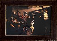Full view of the framed Caravaggio print showing the painting The Calling of Matthew with a dark wooden frame and glass cover.