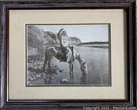 Front view of framed photo print showing Native American man in feather headdress drinking from water while seated on horse by riverside