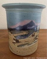 Photo of ceramic vase showing front painted mountain scene with blue sky and earthy colors.