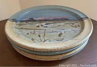 Stacked view of 4 handmade ceramic salad plates displaying blue and beige mountain scene glaze and rustic pottery finish