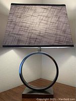 Photo of a contemporary table lamp showing circular metal base and rectangular fabric shade with crosshatch pattern