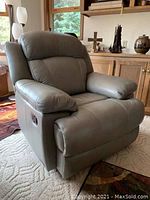 Gray leather recliner chair in upright position showing padded armrests and cushioned backrest in a living room setting.