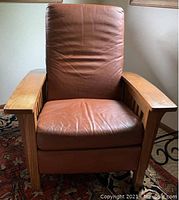 Full front view showing oak arms, slatted sides and leather seat/back.