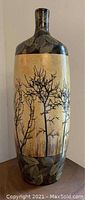 Photo of tall lacquer vase with autumn motif showing bare black tree branches on a tan background, with leaf designs at top and bottom portions of the vase.