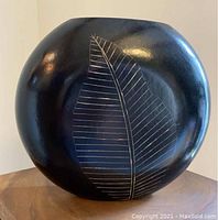Black lacquered wooden vase with a large stenciled leaf design visible on the front, sitting on a wooden surface.