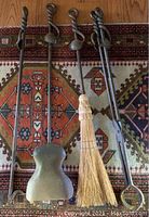 Four fireplace tools including poker, shovel, broom and tongs with twisted handles laid out on a patterned rug.