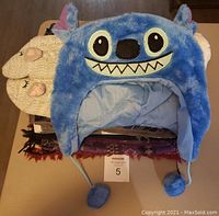 Blue fuzzy Lilo & Stitch character beanie hat with ear flaps and pom-poms; cream colored fuzzy cat socks under the hat