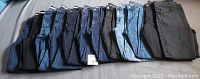 Twelve pairs of women's jeans folded and aligned showing a range of denim colors from dark blue to black to light blue.