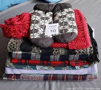 Stack of scarves with fuzzy socks on top, showing knit patterns and colors including beige, black, red, and plaid.