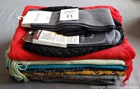 Photo showing the folded scarves in various colors with two pairs of socks on top, one labeled Tabbisocks in grey with black top.