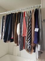 19 pieces of assorted women's clothing hanging on rack including jackets, sweaters, blouses in various colors and patterns.