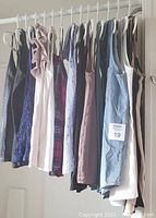 13 women's sleeveless tops hanging on a rack showing an assortment of colors and styles from lace, plaid, solid cotton and silky fabrics.