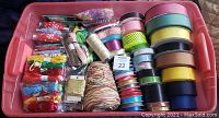 Container bin filled with many ribbon rolls of different types, colors, and sizes including solid and patterned ribbons