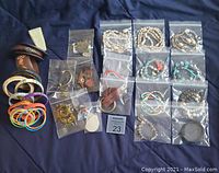 Wide view of assorted fashion jewelry laid out on dark cloth, showing plastic bags with necklaces, earrings, pendants, bracelets, and colorful bands.