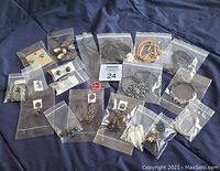 All jewelry pieces organized in individual plastic bags on dark fabric background showing variety of necklaces, bracelets and earrings.