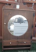 Front view of the brown wooden wall cabinet with round mirror on the door and two small drawers below